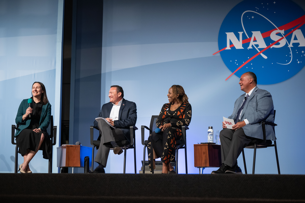 A diverse group of four individuals sits on chairs on a stage.